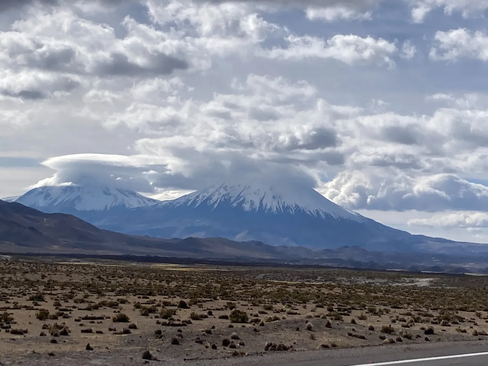 Schneebedeckte Vulkane Sajama und Parinacota unter dichten Wolken im Altiplano